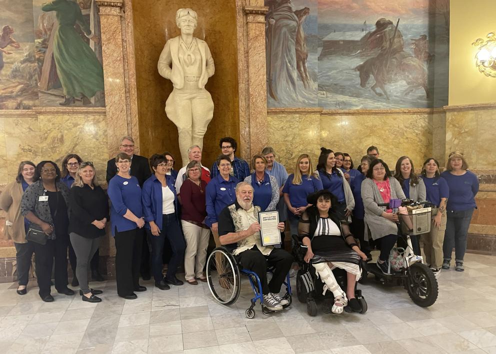 People standing and in wheelchairs pose in front of a statue at the Kansas state Capitol